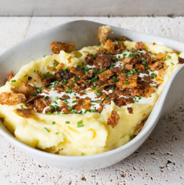 Mashed potatoes in a bowl topped with crème frâiche, crispy potato skin and fresh chives.