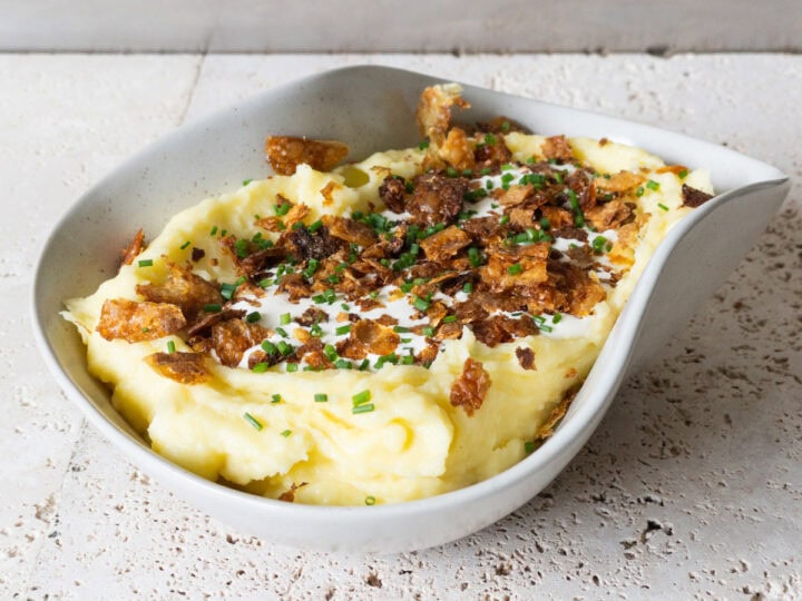 Mashed potatoes in a bowl topped with crème frâiche, crispy potato skin and fresh chives.