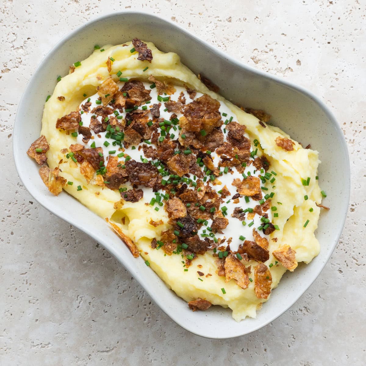 Mashed potatoes in a bowl topped with crème frâiche, crispy potato skin and fresh chives.