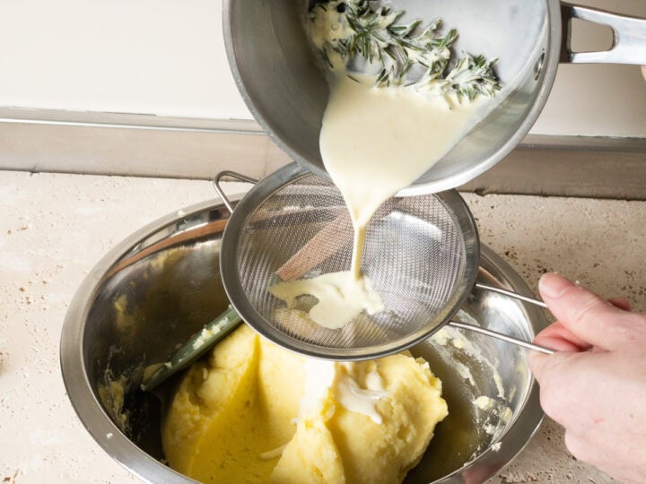 Rosemary infused cream being strained into mashed potatoes in a mixing bowl.