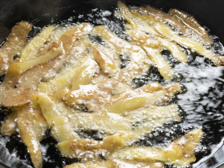 Potato skins frying in hot oil in a skillet.