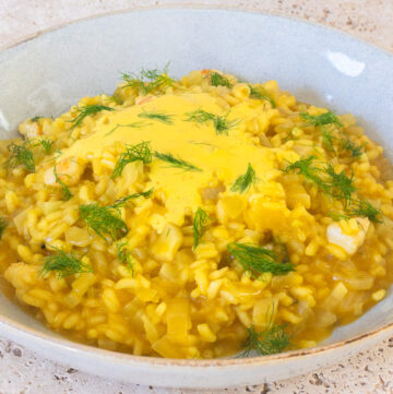 Prawn and saffron risotto served in a blue bowl, topped with a saffron emulsion and fresh fennel fronds to garnish.