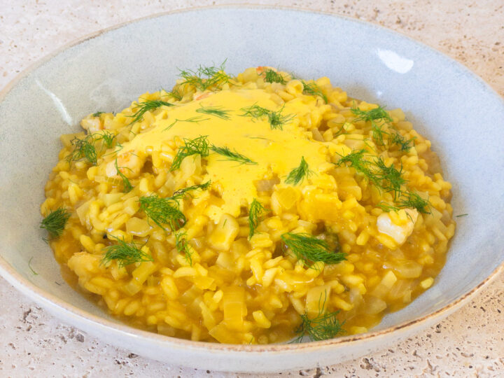 Prawn and saffron risotto served in a blue bowl, topped with a saffron emulsion and fresh fennel fronds to garnish.