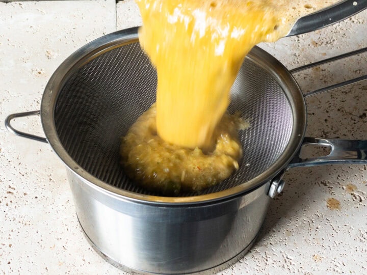 Prawn bisque being strained into a pot through a sieve after being blitzed.