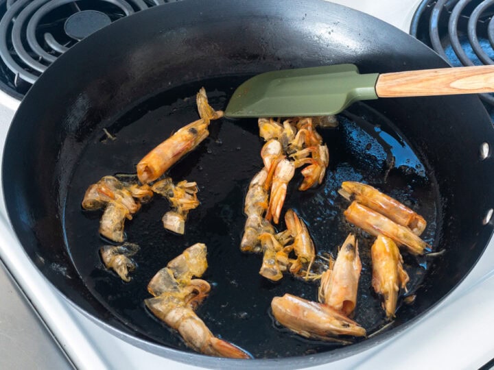 Prawn heads and shells being cooked in olive oil in a skillet over medium heat.