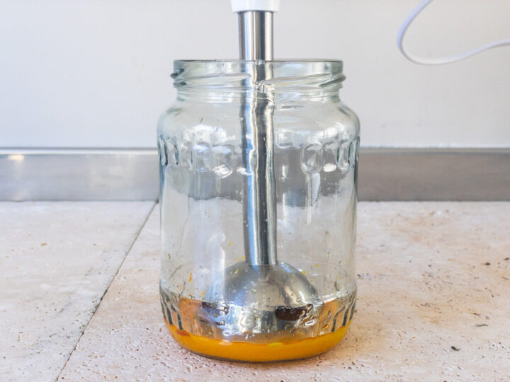 Egg yolk, saffron, garlic and lemon juice being blended in a jar on a bench with an immersion/stick blender.