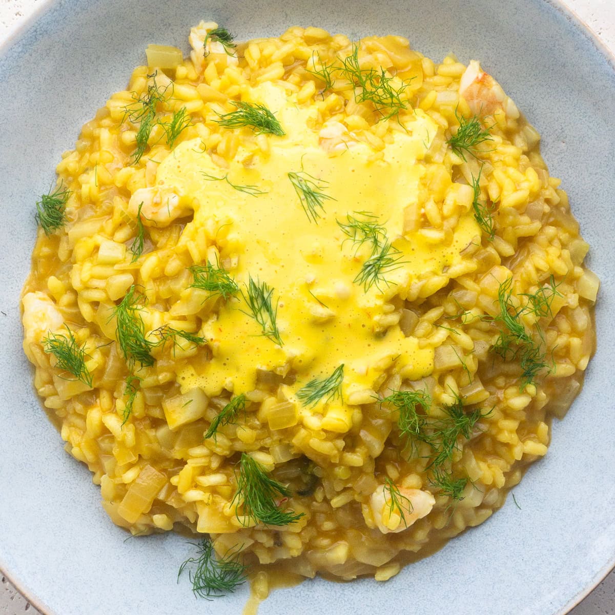 Prawn and saffron risotto served in a blue bowl, topped with a saffron emulsion and fresh fennel fronds to garnish.