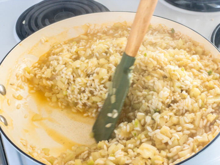 Prawn bisque being stirred through risotto in a pan on the stove.