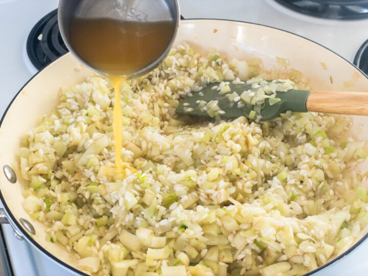 Prawn bisque being added to to arborio rice, diced fennel and onion in a pan on the stove.