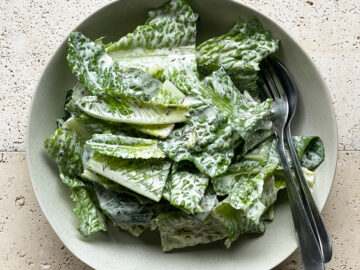 A simple cos lettuce salad dressed with a creamy herb dressing served in a bowl with salad servers.