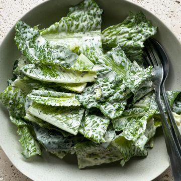 A simple cos lettuce salad dressed with a creamy herb dressing served in a bowl with salad servers.