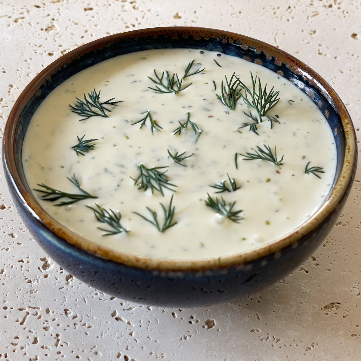 Creamy herb dressing garnished with fresh dill served in a blue ramekin.