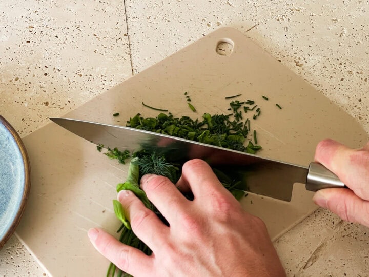 Mixed herbs being finely chopped on a chopping board.