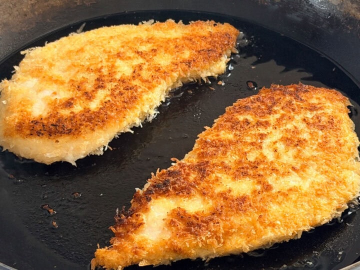 Breaded chicken cutlets cooking in a skillet.