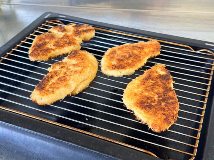 Golden crispy breaded chicken cotoletta on a wire racked oven tray.
