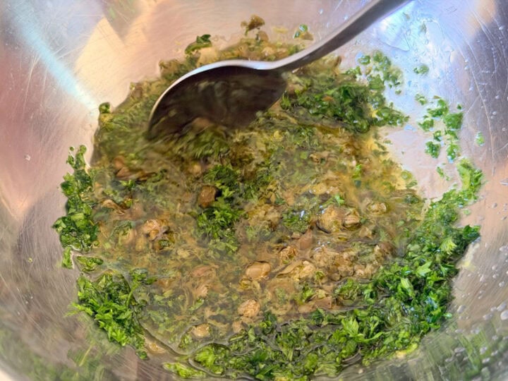 Fresh parsley, capers and lemon zest being mixed with olive oil and lemon juice in a bowl.