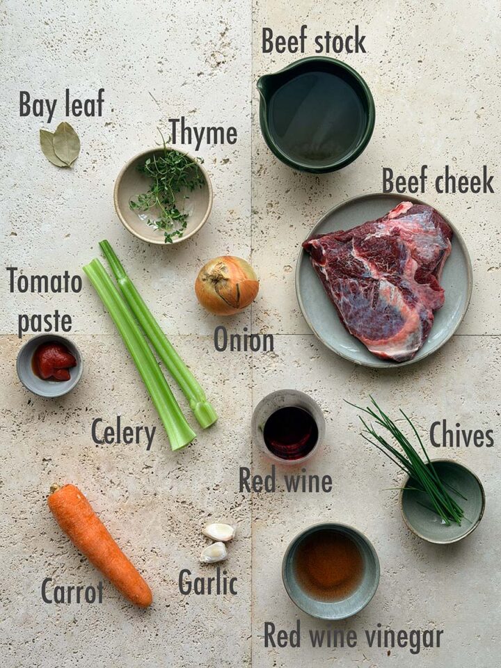 Ingredients for red wine braised beef cheeks: bay leaf, thyme, beef stock, beef cheek, tomato paste, onion, celery, red wine, carrot, garlic, red wine vinegar and chives.