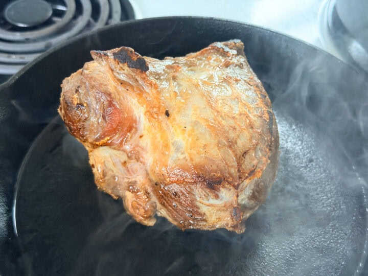 Beef cheek in a hot cast iron pan being browned.