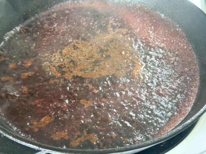 A cast iron skillet being deglazed with red wine after browning meat in it.