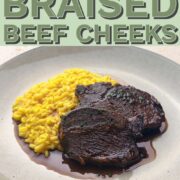 Red wine braised beef cheeks with red wine jus and saffron risotto on a plate.