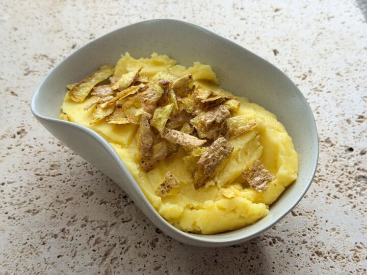 Rosemary mashed potatoes topped with crispy potato skins served in an irregular shaped bowl.