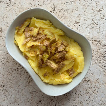 Rosemary mashed potatoes topped with crispy potato skins served in an irregular shaped bowl.