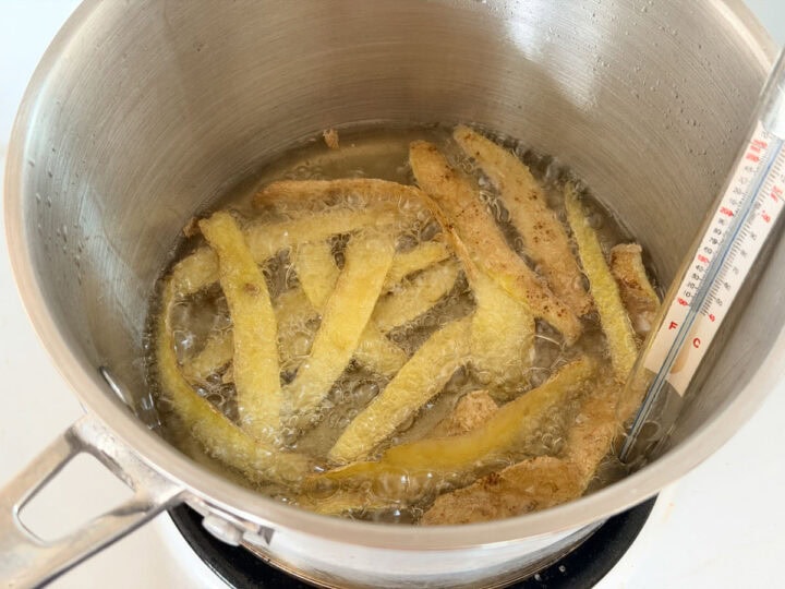 Potato skins frying in hot oil in a pot on a stove.