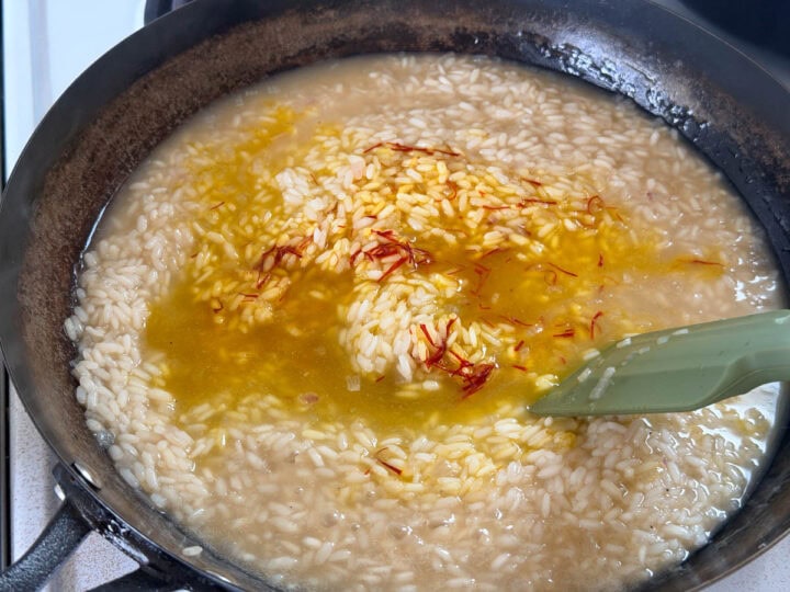 Bloomed saffron is added to a simmering risotto in a pan.