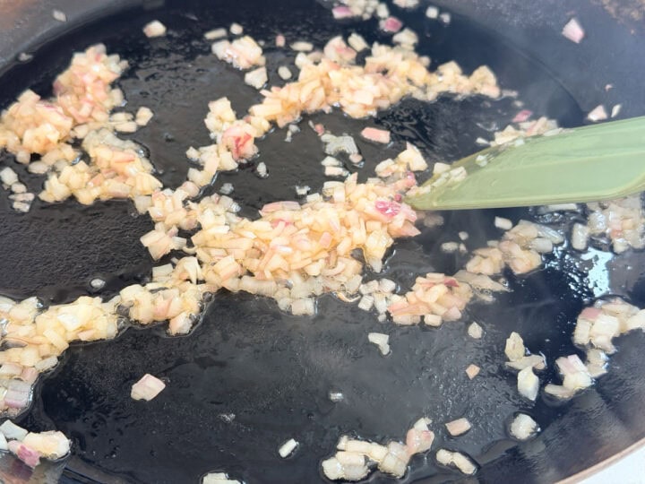 Finely diced shallots being sautéed in a pan.