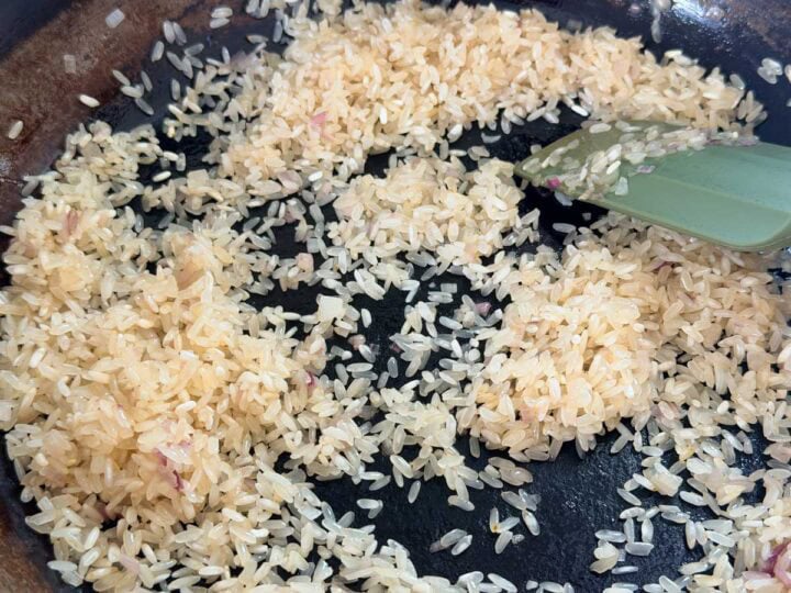 Arborio rice being toasted in a pan with shallots