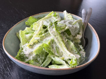 Cos salad with a creamy dill dressing in a bowl with salad servers.