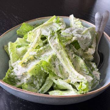 Cos salad with a creamy dill dressing in a bowl with salad servers.