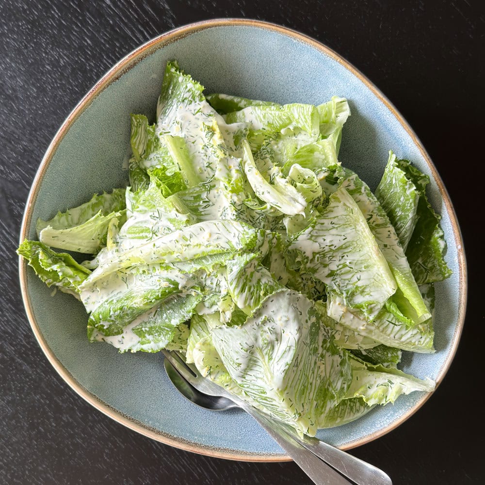 Cos salad with a creamy dill dressing in a bowl with salad servers.